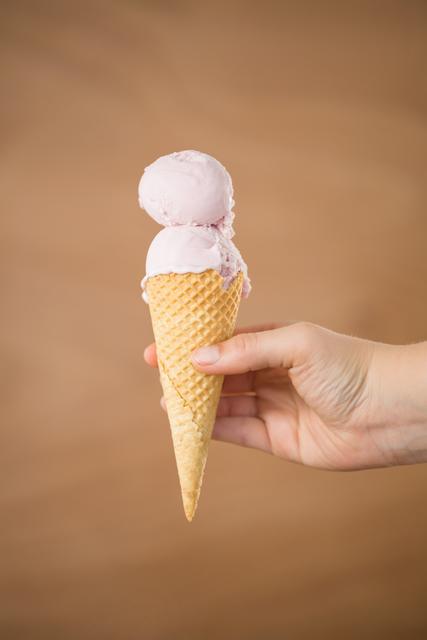 Close-up of hand holding a waffle cone with double scoop strawberry ice cream