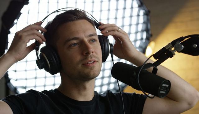 Recording podcast host with headphones speaking into boom microphone and led backlight