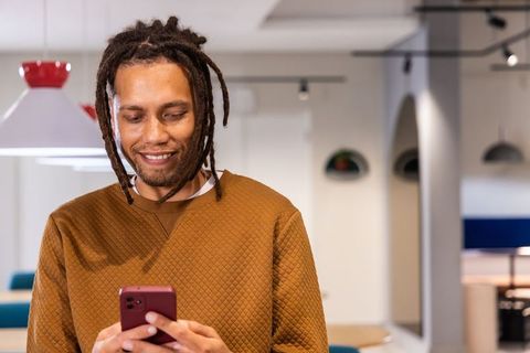 African American man smiling while checking smartphone in modern coworking lounge