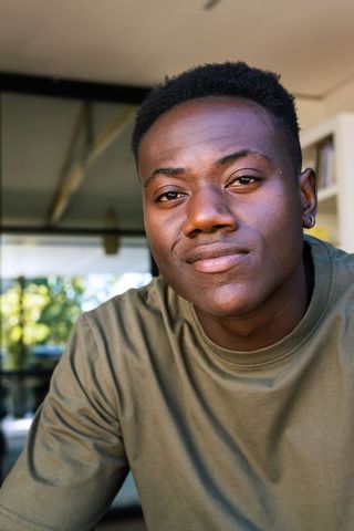 Young man sitting by glass door wearing olive green crewneck, looking calm and thoughtful