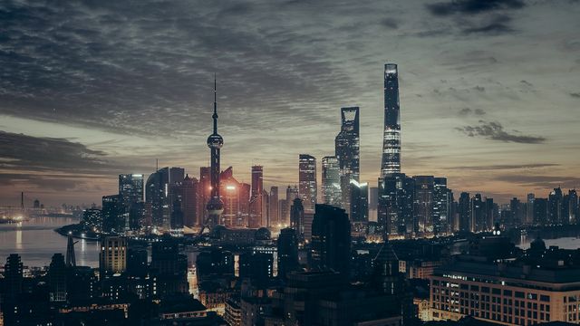 Shanghai's iconic skyline during dusk, showcasing illuminated skyscrapers and a dramatic cloudy sky. Perfect for travel brochures, architecture blogs, urban-themed websites, and tourism advertisements.