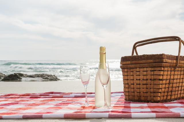 Two glasses, champagne bottle and picnic basket on beach blanket at tropical beach