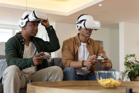 Diverse friends wearing VR headsets playing multiplayer games on sofa in living room