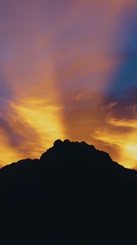Sunset light rising behind mountain ridge casting dramatic rays across colorful sky