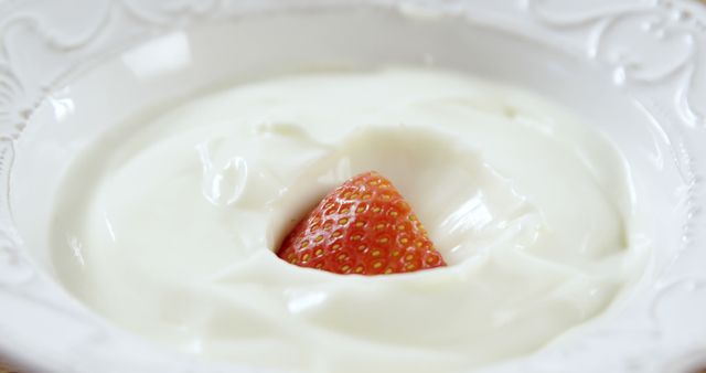 A fresh strawberry is partially submerged in creamy yogurt, with copy space. The contrast of the red berry against the white yogurt creates a simple yet appealing visual treat.