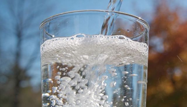Pouring sparkling water into clear glass creating bubbles and sunlit reflections outdoors
