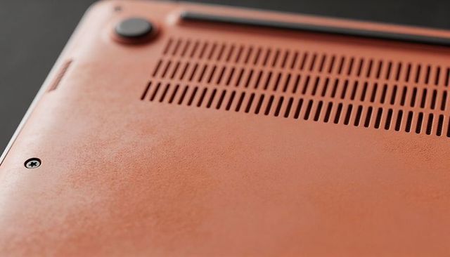 Orange laptop bottom panel closeup showing matte texture ventilation slots and rubber foot