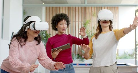 Diverse women exploring virtual reality using VR headsets and tablet in bright lounge
