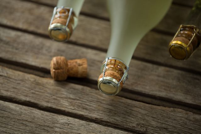 This image captures a close-up view of champagne bottles and a cork on a wooden surface. Ideal for use in advertisements for wine and champagne brands, party invitations, celebration announcements, and luxury lifestyle promotions. The rustic wooden background adds a touch of elegance and sophistication, making it suitable for high-end marketing materials.