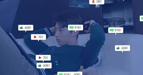 Korean man relaxing with headphones and tablet on couch surrounded by social reactions