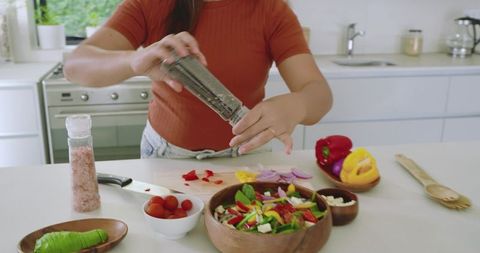 Woman seasoning fresh salad in modern kitchen with pepper grinder