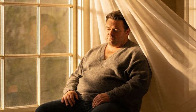 Solitary man sitting by sunlit multipane window in gray sweater contemplating at golden hour