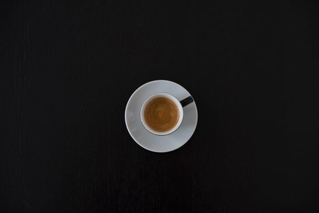Overhead view of an espresso cup on a black background, emphasizing minimalism and simplicity. Perfect for coffee shop promotions, minimalist-themed designs, and lifestyle blogs focusing on coffee culture.