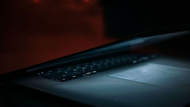 Moody low-key laptop close-up with textured palm rest, backlit keyboard and blue-red light