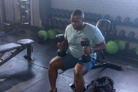 African american man performing seated dumbbell press on adjustable bench in modern gym