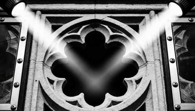 Spotlighting carved quatrefoil on stone facade with metal frames in dramatic monochrome