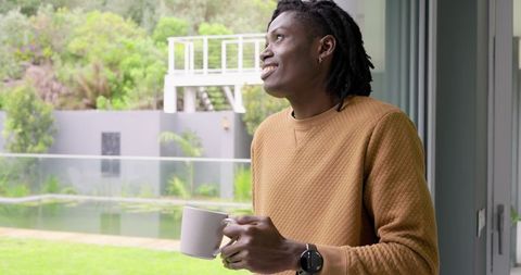Relaxing African American Man Enjoying Morning Coffee by Glass Door Overlooking Backyard Pond