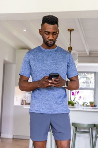 African american man checking smartphone wearing smartwatch in bright modern kitchen