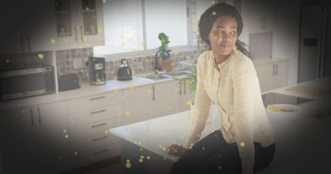 Woman sitting on kitchen island in bright modern kitchen with mosaic tile and houseplant