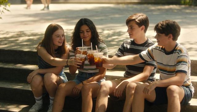 Teen friends toasting iced drinks on park steps wearing striped tees and denim