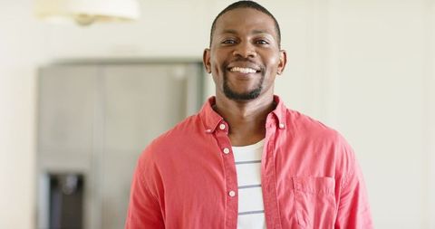 Smiling african american man in modern kitchen wearing coral shirt over striped tee