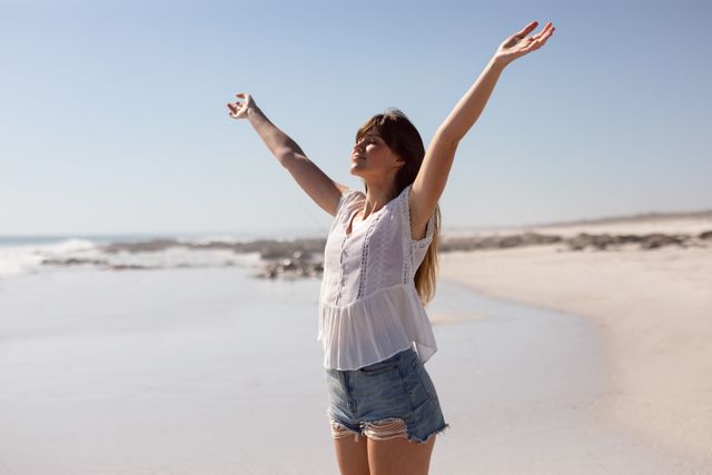 Beautiful young woman with arms stretched out standing on beach in the sunshine