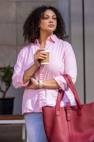 African american woman standing holding coffee, carrying red tote bag in pink shirt