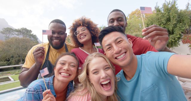 Portrait of happy diverse group of male and female friends holding flags of usa in garden. Friendship, togetherness, celebration and patriotism, unaltered.