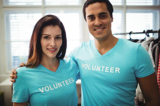 Smiling couple wearing blue volunteer shirts in community workshop. Ideal for promoting volunteer work, community service, teamwork, charity events, and social causes.
