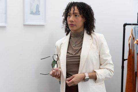 African american woman wearing cream blazer holding glasses in minimalist boutique