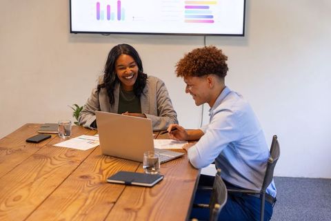Smiling diverse coworkers collaborating over laptop while reviewing charts and analytics