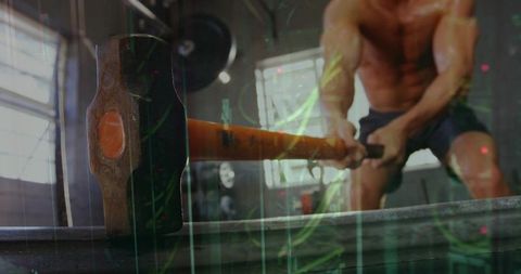 Shirtless athlete swinging sledgehammer powering explosive garage gym workout