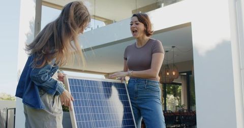 Diverse women lifting and examining solar panel on modern porch promoting renewable energy