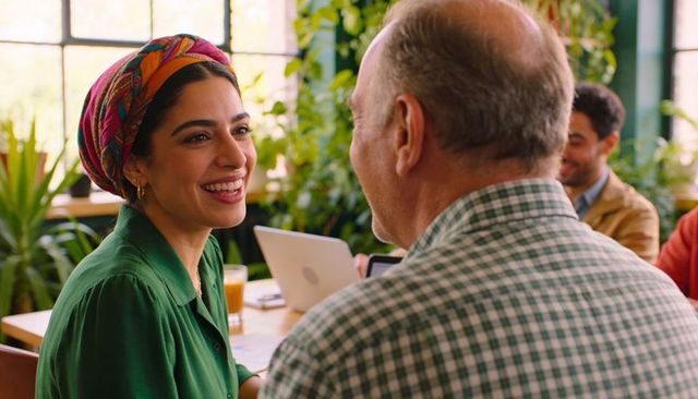 Smiling woman wearing colorful headscarf chatting in sunlit plant-filled coworking cafe
