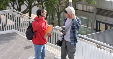 Multicultural college students chatting on urban campus stairs with notebooks and coffee