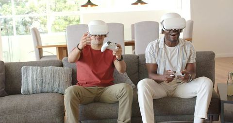 Multiracial friends wearing white VR headsets playing immersive couch gaming together