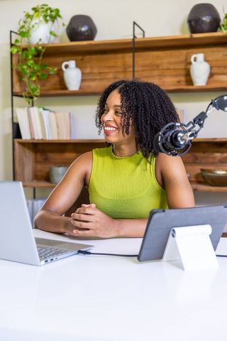 African american female recording podcast in bright home office with laptop and microphone