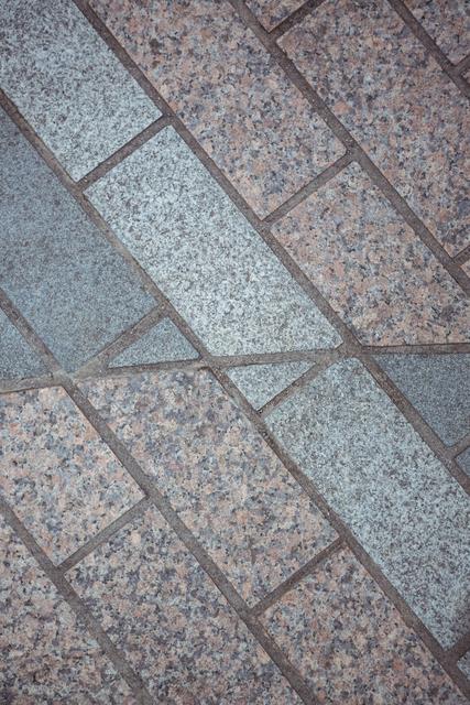 Close-up view of interlocking paving stones forming a geometric pattern. Ideal for use in architectural designs, urban planning presentations, construction materials catalogs, and as a background for various design projects.