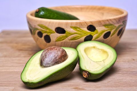 Halved Avocado Showing Seed with Decorative Olive-Leaf Carved Wooden Bowl on Cutting Board
