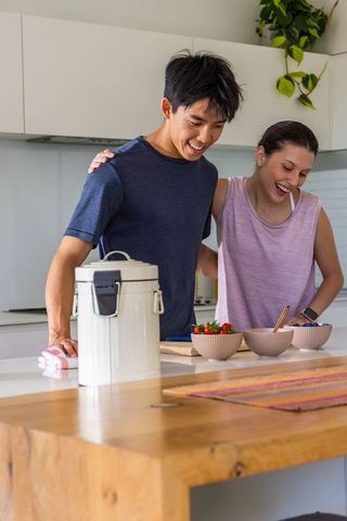 Diverse couple preparing healthy breakfast bowls at kitchen island, smiling together