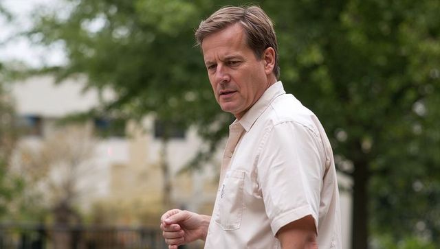 Middle-aged man standing in urban courtyard turning left wearing beige short-sleeve shirt