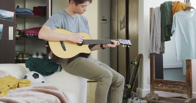 Asian boy playing guitar sitting on the couch at home. teenager lifestyle and living concept
