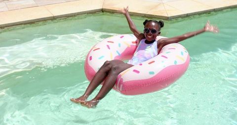 Joyful african american girl on pink donut float in pool