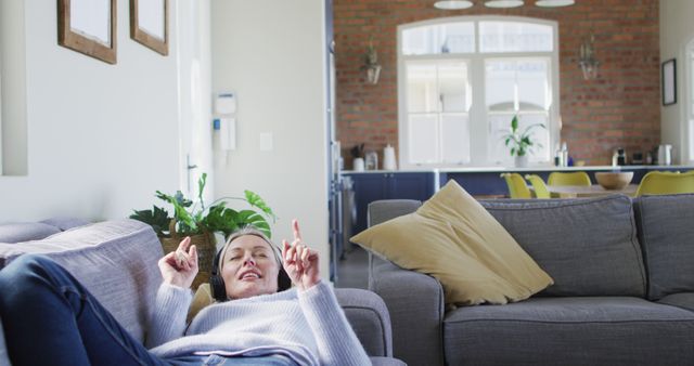 Relaxed senior caucasian woman in living room lying on sofa, wearing headphones. retirement lifestyle, at home with technology.
