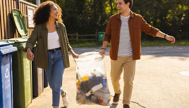 Couple carrying recyclables while walking to recycling bins during sunny community cleanup