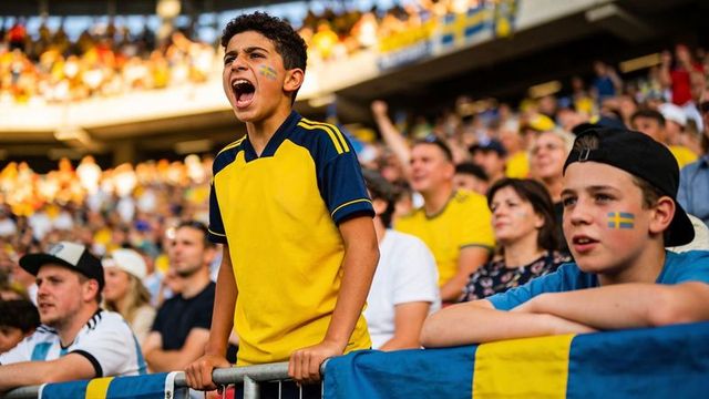 Teen swedish fans cheering loudly at stadium front rail, face paint, yellow jerseys