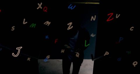 Standing male silhouette holding smartphone amid floating neon letters and glowing glyphs