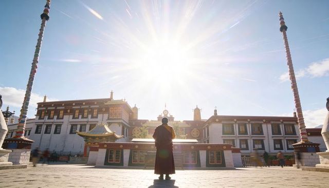 Solitary monk standing at tibetan monastery courtyard under radiant sunlight with gold roofs and pra