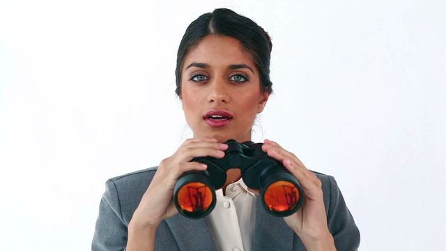 A professional businesswoman holding binoculars, showing concentration. Suitable for use in themes related to business, focus, corporate strategy, future planning, and career growth. Useful for business presentations, marketing materials, and corporate websites.