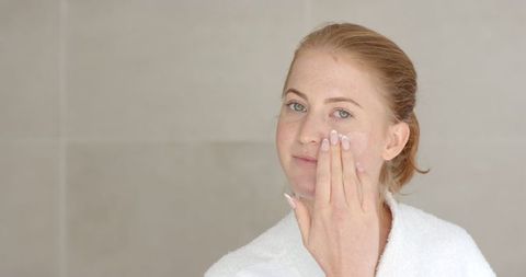 woman applying facial cream wearing bathrobe - Download Free Stock Images Pikwizard.com
